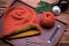 a knitted hat sits on a tray next to some knitting needles and balls of yarn