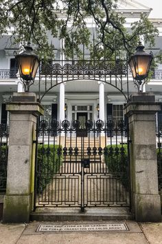 an iron gate with two lamps on each side in front of a large white building