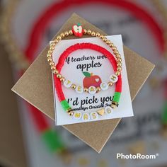 a red beaded bracelet with an apple on it and the words teachers wear apples i'd pick you