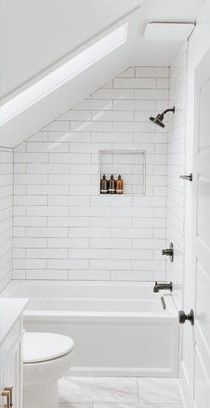 an attic bathroom with white tile and black fixtures, along with a toilet and bathtub