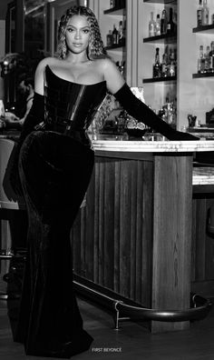 a black and white photo of a woman standing in front of a bar with bottles on the shelves