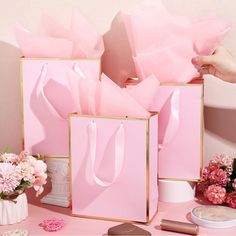 pink shopping bags are sitting on a table next to flowers and other items in front of them