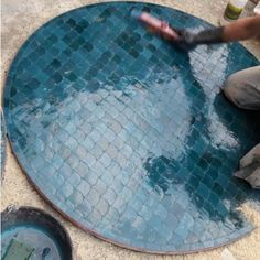 a man is working on a blue mosaic tile floor in the middle of a pool