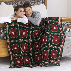 a man and woman laying on top of a bed covered in a crocheted blanket