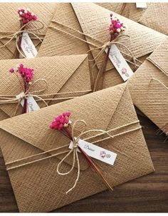 several envelopes tied together with twine and pink flowers are shown on a wooden table