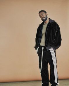 a man standing in front of a beige wall wearing black and white tracksuits