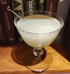 a drink in a glass on top of a wooden table next to books and a bookcase