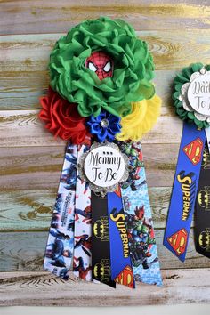 two ribbons with the words, mommy to be and spiderman on them are hanging from a wooden wall