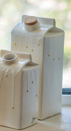 two white ceramic jugs sitting next to each other on a window sill in front of a window