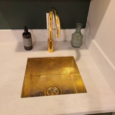 a gold sink in a bathroom next to a bottle and soap dispenser