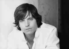 a black and white photo of a young man with long hair wearing a white shirt