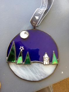 a purple and white ornament with a small house in the mountains on it