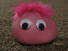 a close up of a pink rock with eyes and hair on it's face