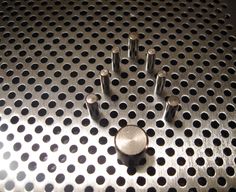 a metal grate with holes in the middle and one hole at the top that has several fingers on it