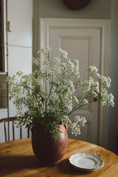 a vase with white flowers sitting on top of a wooden table next to a plate