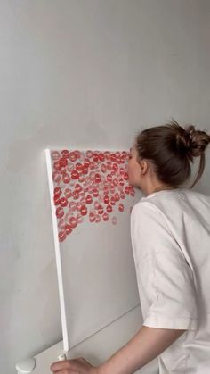 a woman leaning against a white wall with red circles on it