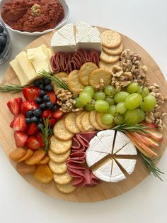 a wooden platter filled with cheese, crackers and fruit