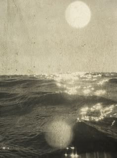 an old photo of the ocean with waves coming in to shore and sun shining through the clouds