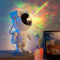 a small toy astronaut is standing on top of a desk next to a laptop computer