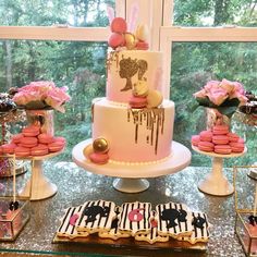 a table topped with lots of pink and white desserts next to a large window