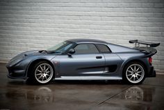 a gray sports car parked in front of a brick wall