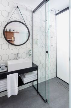 a bathroom with white hexagonal tiles on the wall and black countertop, along with a round mirror