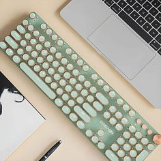 a computer keyboard sitting on top of a desk next to a laptop and a pen