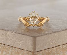 a gold ring with a heart shaped diamond on top of a silver box next to it