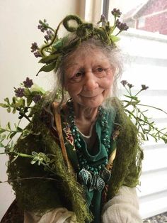 an old woman with flowers on her head and green scarf around her neck, sitting in front of a window