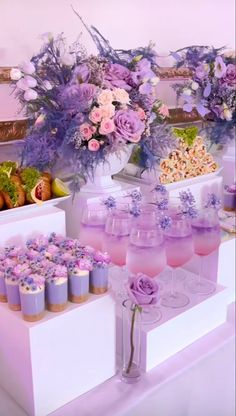 there are many desserts on the table with purple frosting and flowers in vases