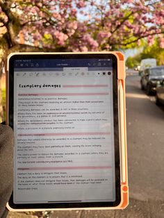 someone is holding up a tablet computer in front of a tree with pink flowers on it