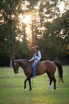 a young woman riding on the back of a brown horse in a grassy field at sunset