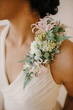 a woman wearing a white dress holding a bouquet of flowers and greenery on her shoulder