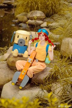 a woman sitting on top of a rock next to a river holding a skateboard