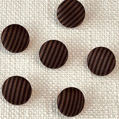 four brown buttons sitting on top of a white fabric covered table cloth with black pins