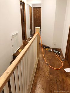 an orange hose is connected to the top of a wooden railing in a hallway with hard wood flooring