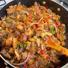 a skillet filled with meat and vegetables on top of a stove burner next to a wooden spatula