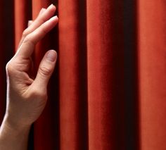 a hand reaching out from behind a red curtain to touch the curtains with their fingers