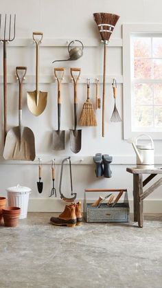 a bunch of gardening tools hanging on the wall next to a table and chair in front of a window