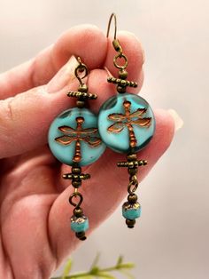 a pair of blue earrings with gold dragonflys hanging from it's ear wires