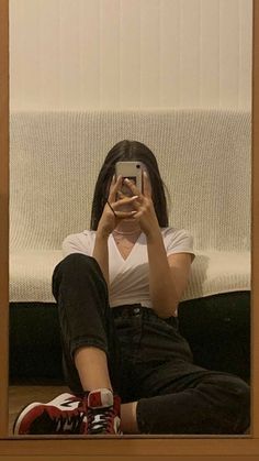 a woman sitting on the floor taking a selfie in front of a mirror with her cell phone