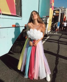 a woman standing in front of a bus wearing a rainbow colored dress and white sneakers