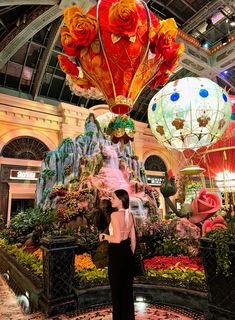 a woman standing in front of a display of flowers and hot air balloons at a mall