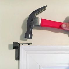 a hand holding a hammer over a white door with a red handle and black bar