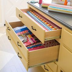 an open drawer in a kitchen next to a counter top with books and pencils on it