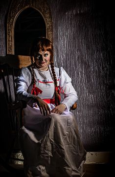 a woman sitting on top of a wooden chair in front of a mirror wearing clown makeup