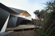 an unusual house in the woods is made out of black and white materials, with a wooden platform leading to it