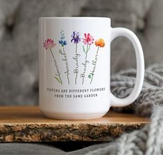 a white coffee mug with flowers on it sitting on a wooden table next to a gray blanket