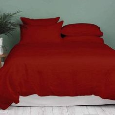 a bed with red sheets and pillows in a room next to a potted plant