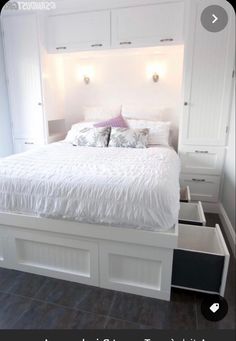 a white bed with drawers underneath it in the middle of a floored room,